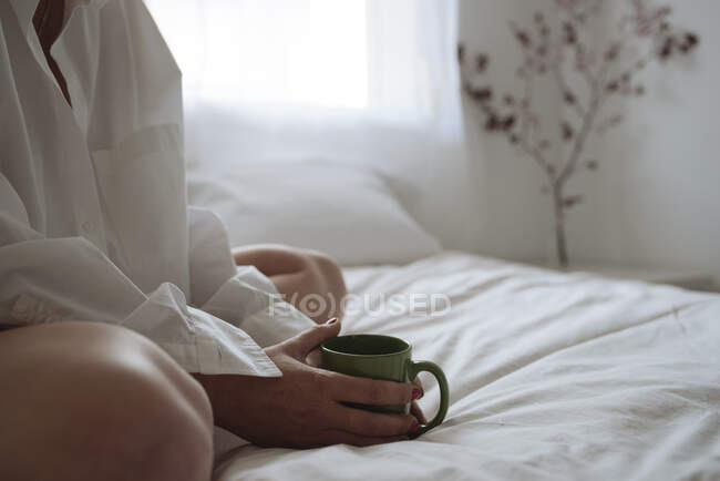 Close up of hands holding a cup of coffee on the bed — Stock Photo