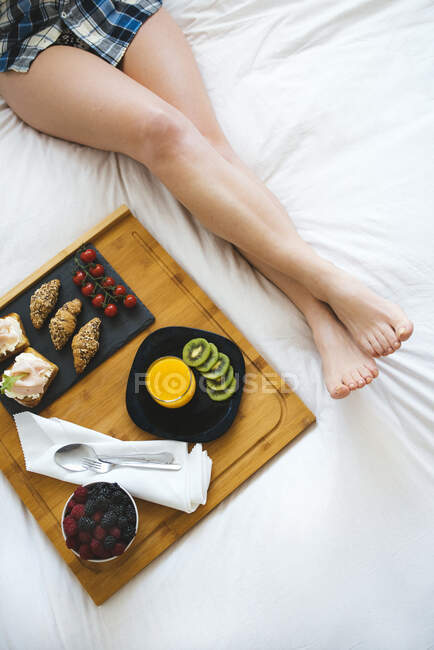 Close up of female legs and breakfast tray on bed in white bedroom — Stock Photo