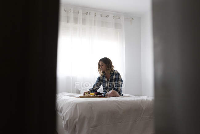 View thru a door ajar of woman having breakfast on bed. — Stock Photo