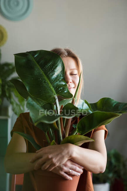 Mujer abraza planta en maceta con hoja grande que cierra su mitad de la cara - foto de stock