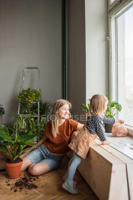 Femme s'assoit et regarde la fenêtre, petite fille près des points par la fenêtre. — Photo de stock
