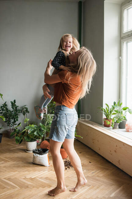 Donna tiene in abbracci il suo bambino ridente in soggiorno con molte piante — Foto stock
