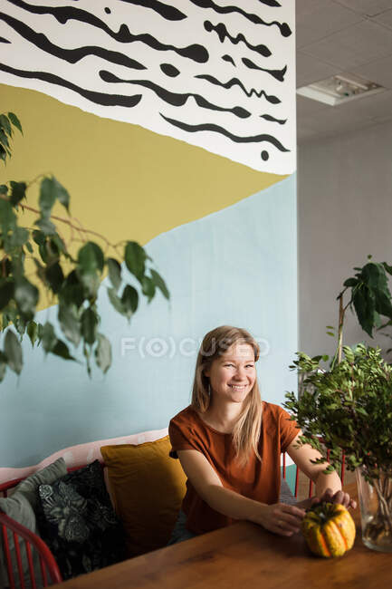 Жінка сидить на дивані в оточенні рослин, дивиться на камеру з посмішкою . — стокове фото