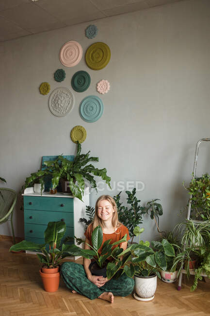 Donna felice siede in posa loto sul pavimento circondato da piante in vaso — Foto stock