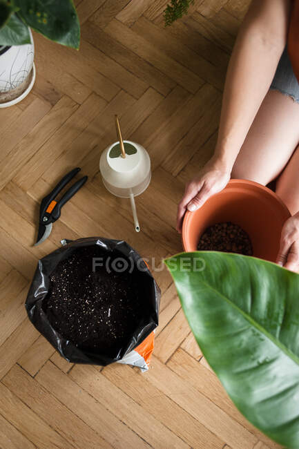 Mujer mantenga olla con drenaje al lado del suelo y regadera en el suelo - foto de stock