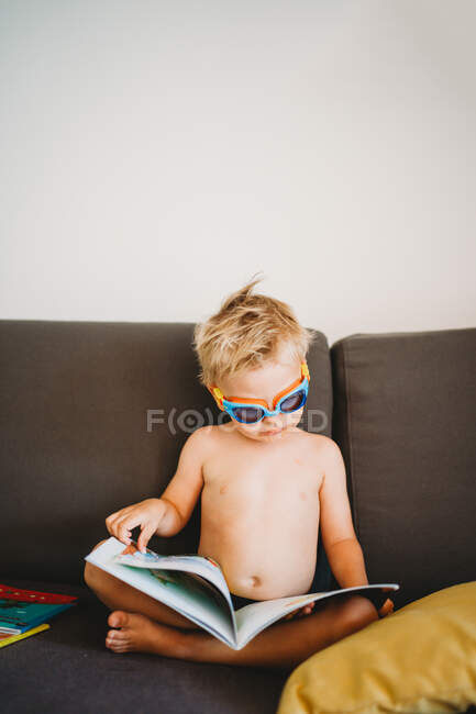 Young male toddler reading topless with goggles for homeschooling — Stock Photo