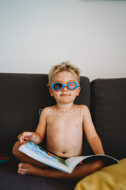 Jeune garçon lisant avec des lunettes pour l'école à domicile en regardant la caméra — Photo de stock