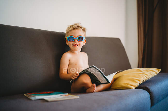 Male child reading topless with goggles and sticking his tongue out — Stock Photo