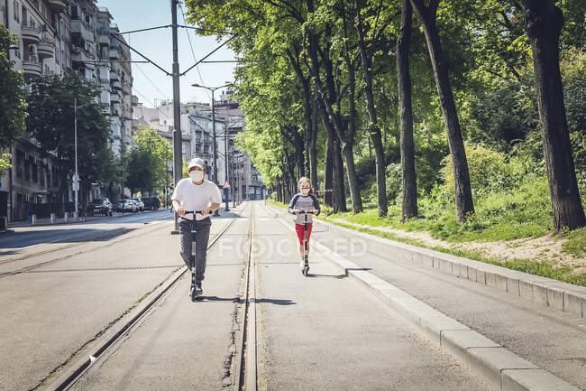 Irmão e irmã vestindo máscaras montando Scooters em Belgrado, Sérvia — Fotografia de Stock