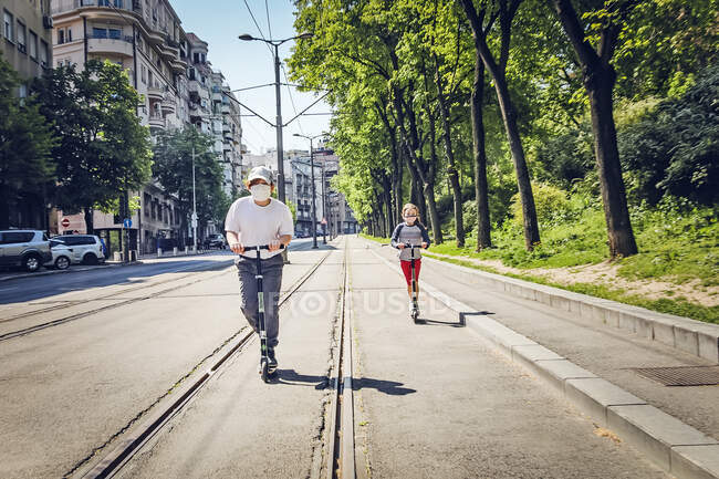 Двое детей едут на скутерах и носят маски в Белграде, Сербия — стоковое фото