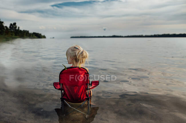 Маленькая девочка сидит в кресле на пляже в летний день — стоковое фото
