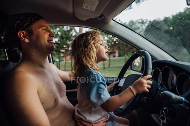 Hija fingiendo conducir coche en el regazo de los papás - foto de stock