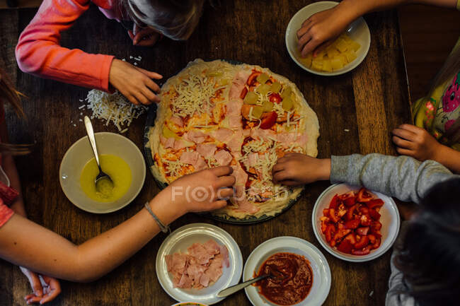 Crianças fazendo pizza caseira para jantar juntas na mesa — Fotografia de Stock