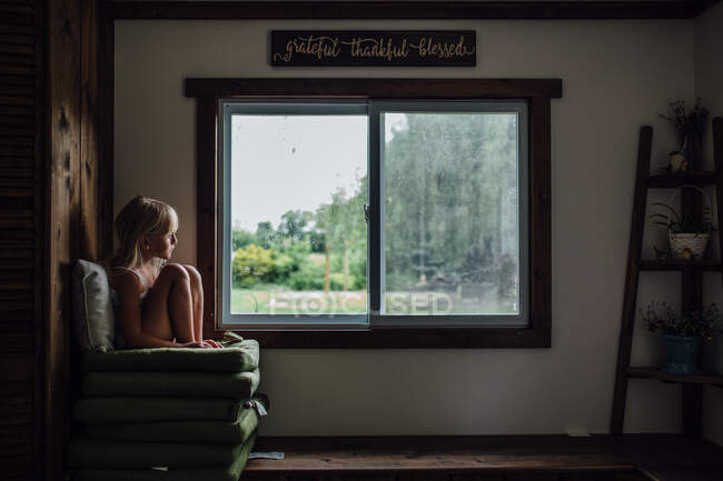 Menina sentada na cadeira pela janela em casa — Fotografia de Stock