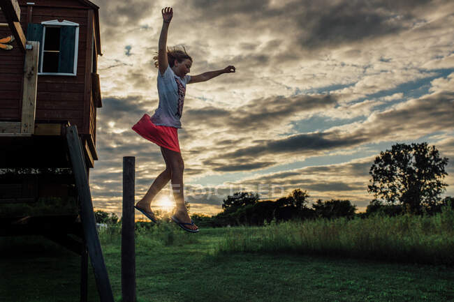 Girl jumping off of tree house swing set in yard — Stock Photo