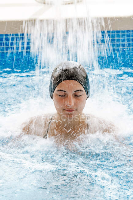 Young beautiful girl eyes closed, relaxing under a waterfall in a spa — Stock Photo
