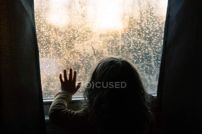 Menina criança olhando para o pôr do sol através de uma janela. — Fotografia de Stock