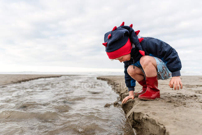 Little kid in boots playing with sand in New Zealand — Stock Photo