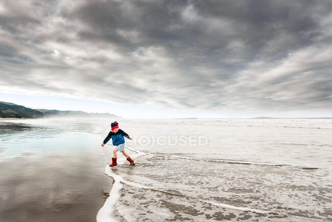 Criança correndo na água na praia da Nova Zelândia na tarde nublada — Fotografia de Stock