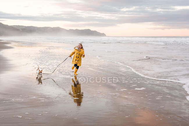 Happy tween girl running with dog at beach in New Zealand — Stock Photo
