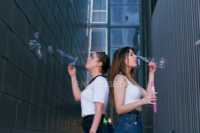 Two women, young friends have fun making soap bubbles in a big city alley — Stock Photo