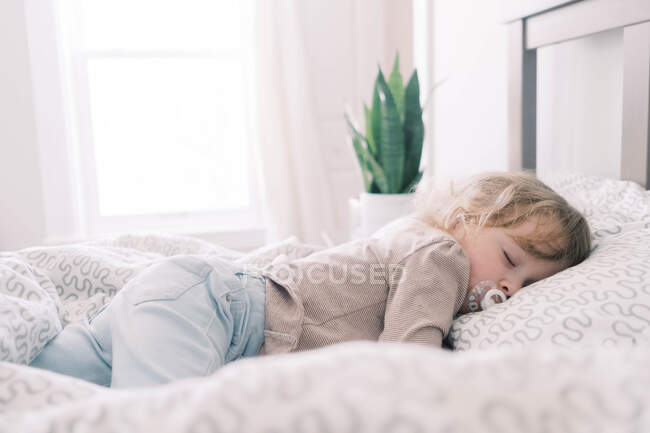 A toddler sleeping in her parents bed with a pacifier. — Stock Photo