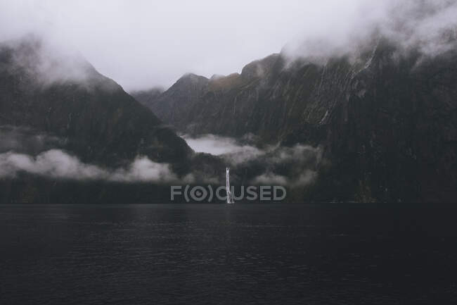 Сценический вид водопада на горы в Милфорде во время туманного дня, Новая Зеландия — стоковое фото