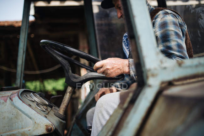 Viejo granjero conduciendo un tractor. - foto de stock