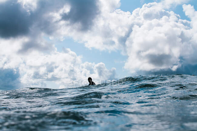 Surfista sentado solo bajo un cielo malhumorado en el océano - foto de stock