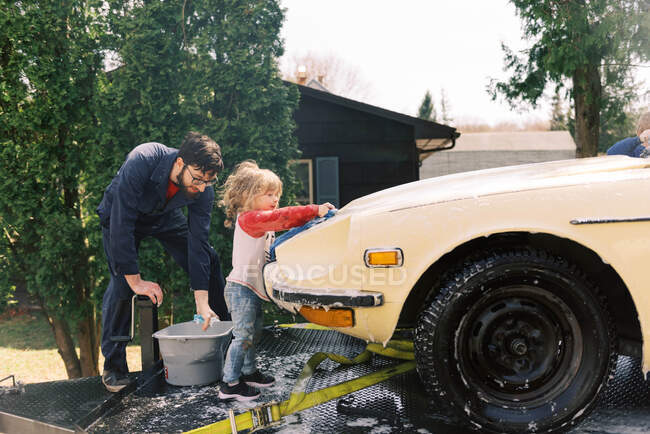 Father and his toddler daughter washing a classic car together — Stock Photo
