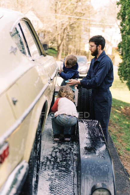 Um pai e sua filha criança lavando um carro clássico juntos. — Fotografia de Stock