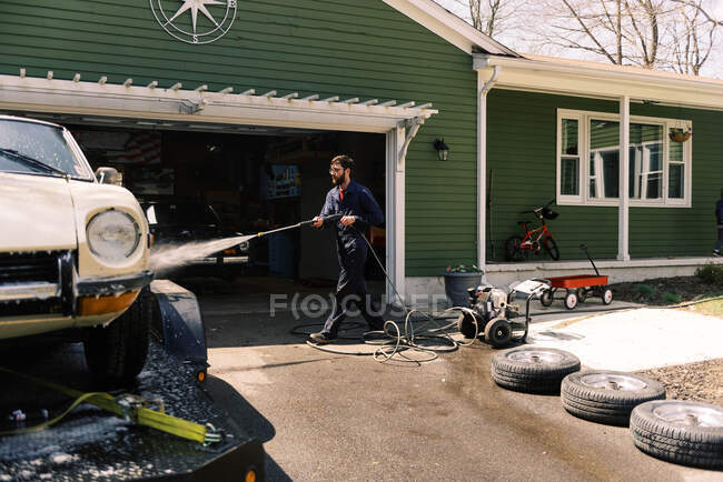 Un macho milenario usando una lavadora de energía para limpiar su coche. - foto de stock