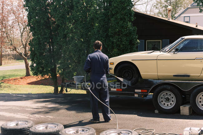 A millennial male using a power washer to clean his car. — Stock Photo