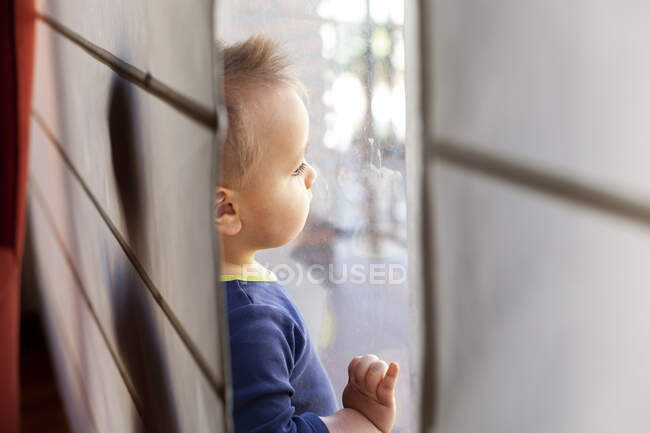 Portrait of little blond boy looking through window — Stock Photo