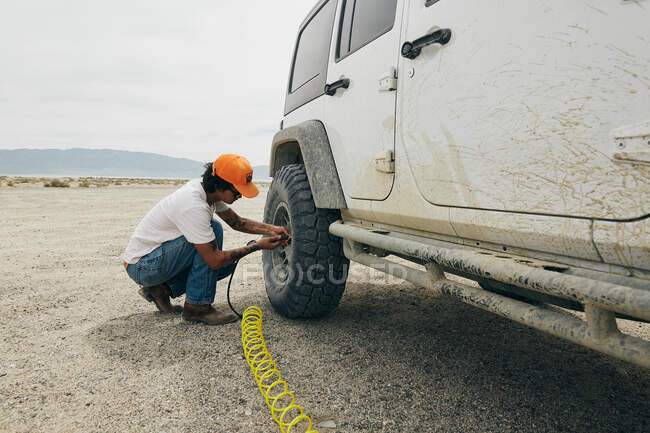 Joven poniendo aire en los neumáticos durante el viaje por carretera. - foto de stock