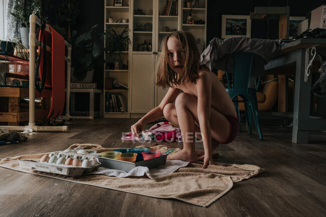 Молодая девушка раскрашивает пасхальные яйца одна в комнате — стоковое фото