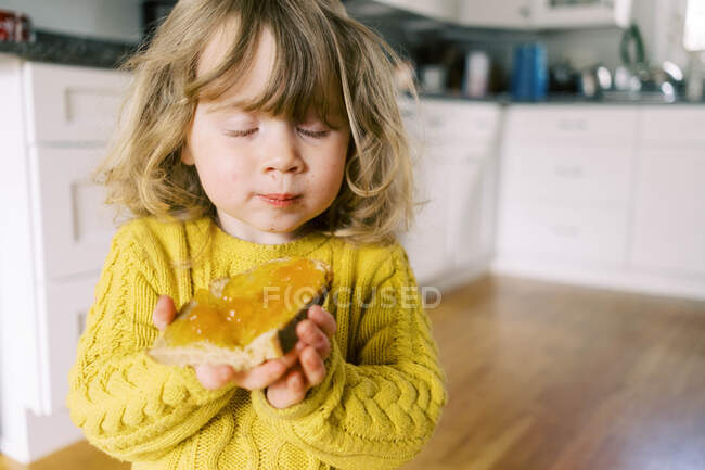 Pequeña niña disfrutando de un pan recién horneado con mermelada de albaricoque. - foto de stock