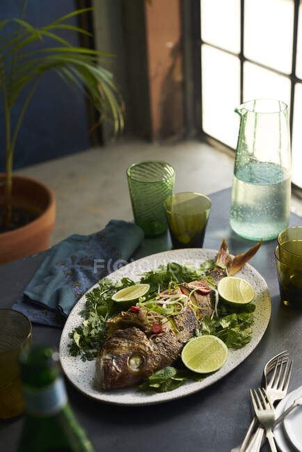 Plato de pescado entero asado en un entorno de mesa con vasos y servilleta - foto de stock