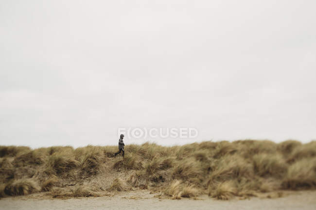 Хлопчик біжить піщаною дюною в похмурий зимовий день — стокове фото