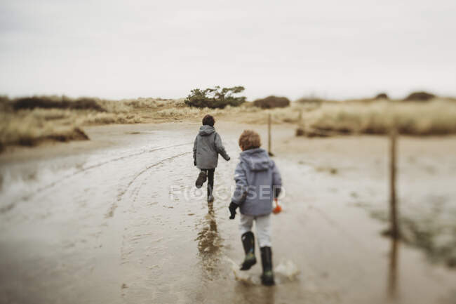 Dois meninos no inverno correndo através de poças em areia duna saltmarsh — Fotografia de Stock