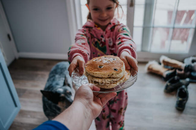 Porträt einer Person, die einem kleinen Mädchen im Pyjama Pfannkuchen reicht — Stockfoto