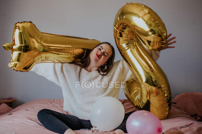Tween menina sentada em sua cama brincando com balões de grande número — Fotografia de Stock