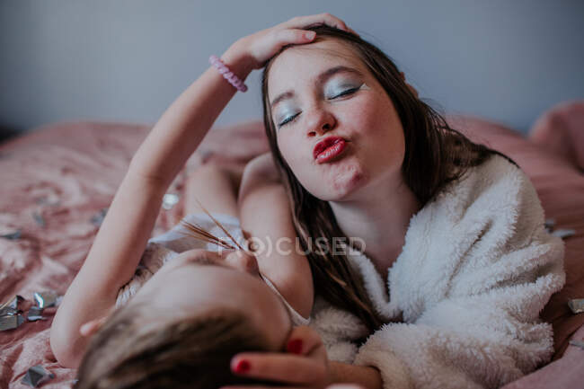 Сестри лежать на ліжку, роблячи обличчя гофрованими разом — стокове фото