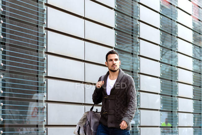 Jeune homme barbu marchant dans la rue à côté de l'immeuble de bureaux — Photo de stock