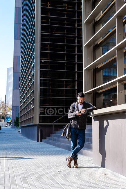Homme utilisant un smartphone à l'extérieur, debout à côté de l'immeuble de bureaux — Photo de stock