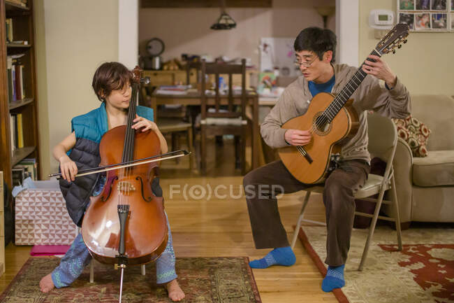 A tween boy and his father play music together in living room at home — Stock Photo