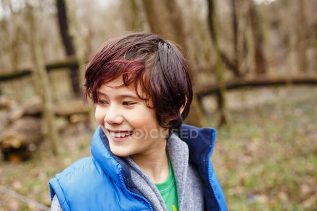 Un niño sonriente mira a un lado mientras está de pie en el bosque en primavera - foto de stock