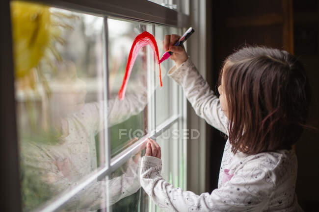Ein kleines Kind zeichnet eine helle Sonne und einen Regenbogen auf eine Fensterscheibe — Stockfoto