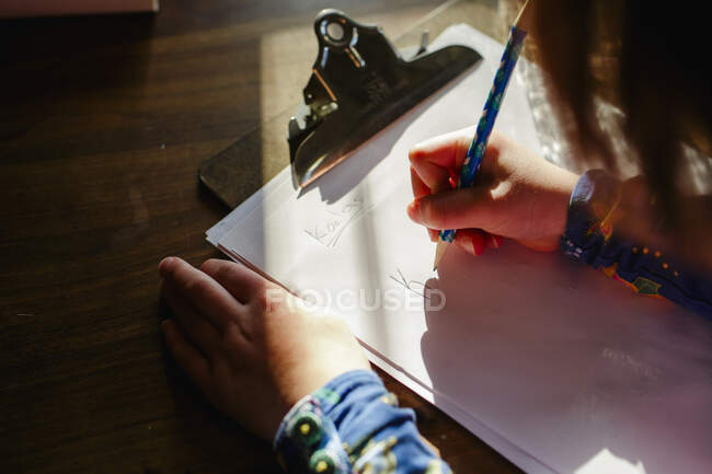 Close-up of a small child sitting in a patch of light doing homework — Stock Photo