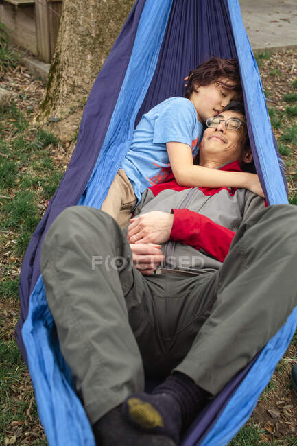 A happy child cuddles his smiling father in a hammock outside — Stock Photo